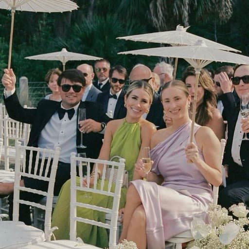Wedding guests holding champagne under white parasols at an outdoor reception
