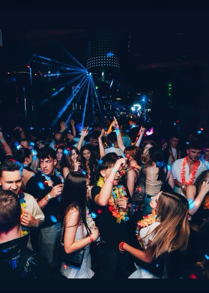 Party guests in flower leis dancing under neon lights