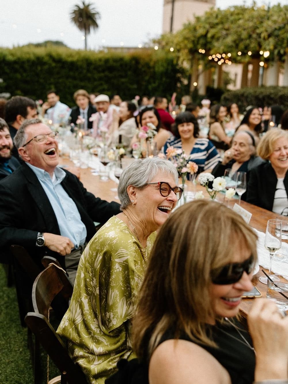 Wedding guests laughing at a long candlelit table at a garden reception